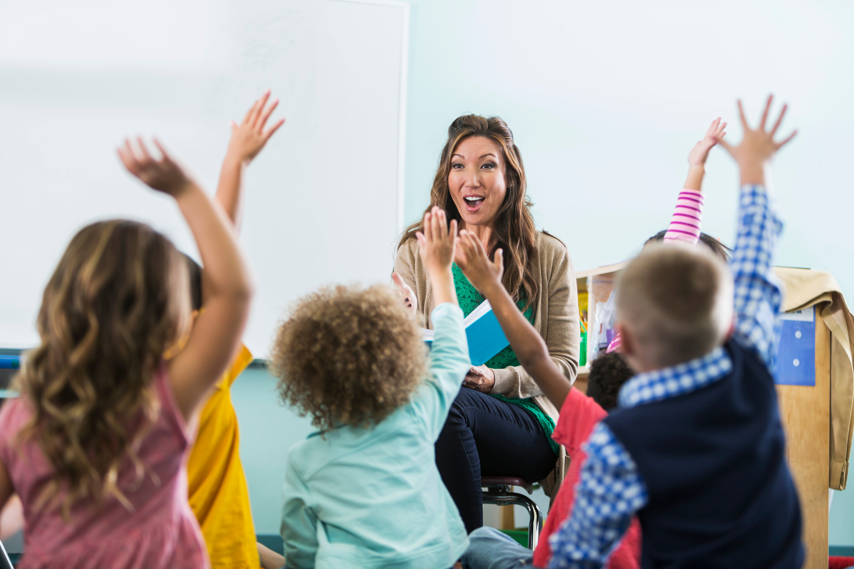 Preschool teacher, children raising hands in class